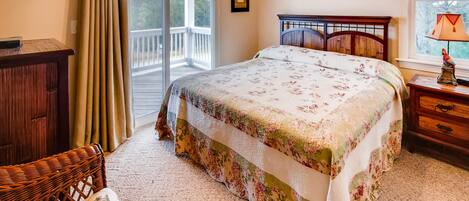 A bedroom with a bed, a wooden nightstand, a wicker chair, a wooden dresser, and a window with a view of trees.