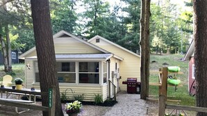 Ein kleines, eingeschossiges Haus mit Veranda, Grill und Holzzaun.