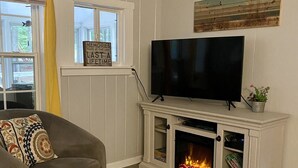 Ein Wohnzimmer mit grauem Sofa, Kamin, Flachbildfernseher und Fenster mit gelbem Vorhang.
