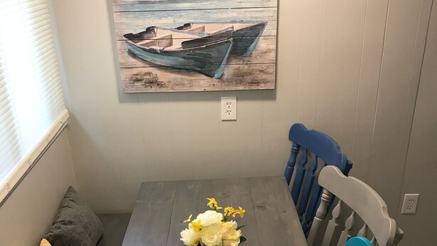 Una mesa de comedor con un centro de mesa floral, sillas azules y grises, y un cuadro de un barco en la pared.