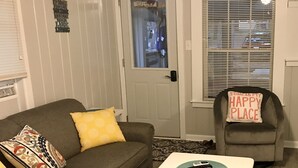 A living room with a brown couch, a white door, and a chair with a pillow labeled "HAPPY PLACE".