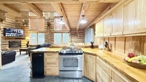 Interior de una cabaña de troncos con cocina que incluye estufa, pileta y armarios de madera.