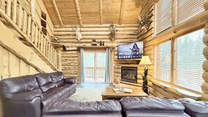 Interior de una cabaña de troncos con un sofá de cuero, chimenea y televisión.