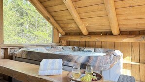 Una cabaña de madera con un jacuzzi, un banco de madera y una bandeja con copas de vino y uvas.