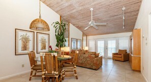 A spacious living area with a high ceiling, a dining table with chairs, a sofa, and a ceiling fan.