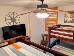 A bedroom with a bed, a TV, a ceiling fan, a wooden wall, and a window. - SUMMER ALERT - Steps to Hot Tub - Family friendly (Eden)