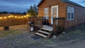 Une petite cabane en bois avec une véranda, un barbecue et un foyer.