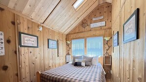 Une pièce chaleureuse, aménagée dans une cabane en bois, avec un lit, une petite table et des tableaux encadrés accrochés aux murs.