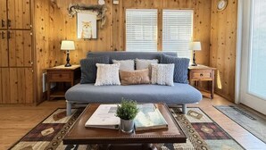 Une pièce chaleureuse avec un plafond en bois, un canapé bleu agrémenté de coussins à motifs, deux tables de chevet avec des lampes et une table basse sur laquelle est posée une plante.