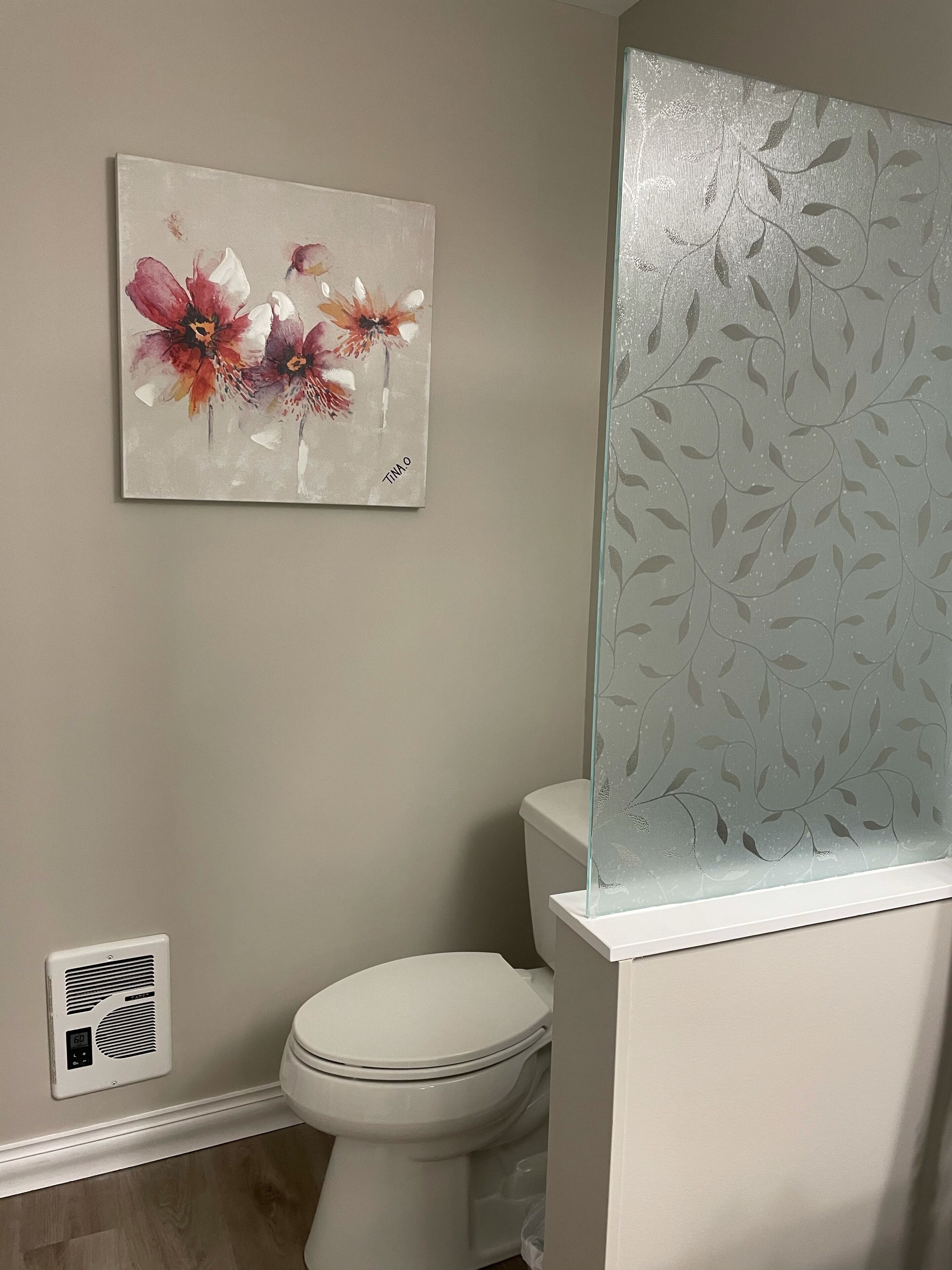 A bathroom with a toilet, a wall-mounted artwork of flowers, and frosted glass panels.