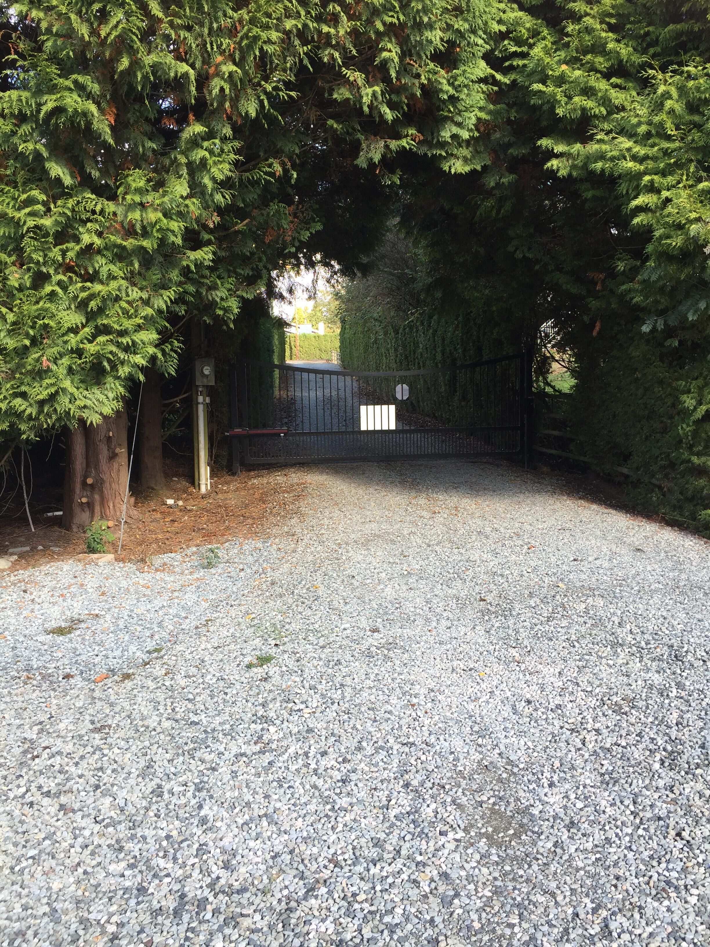 Un camino de grava que conduce a una zona vallada con una puerta metálica y una señal de stop.