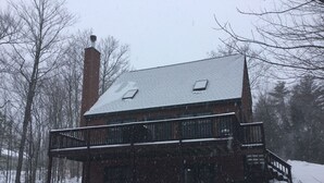 Eine zweistöckige Holzhütte mit Schornstein, Balkon und überdachter Veranda.