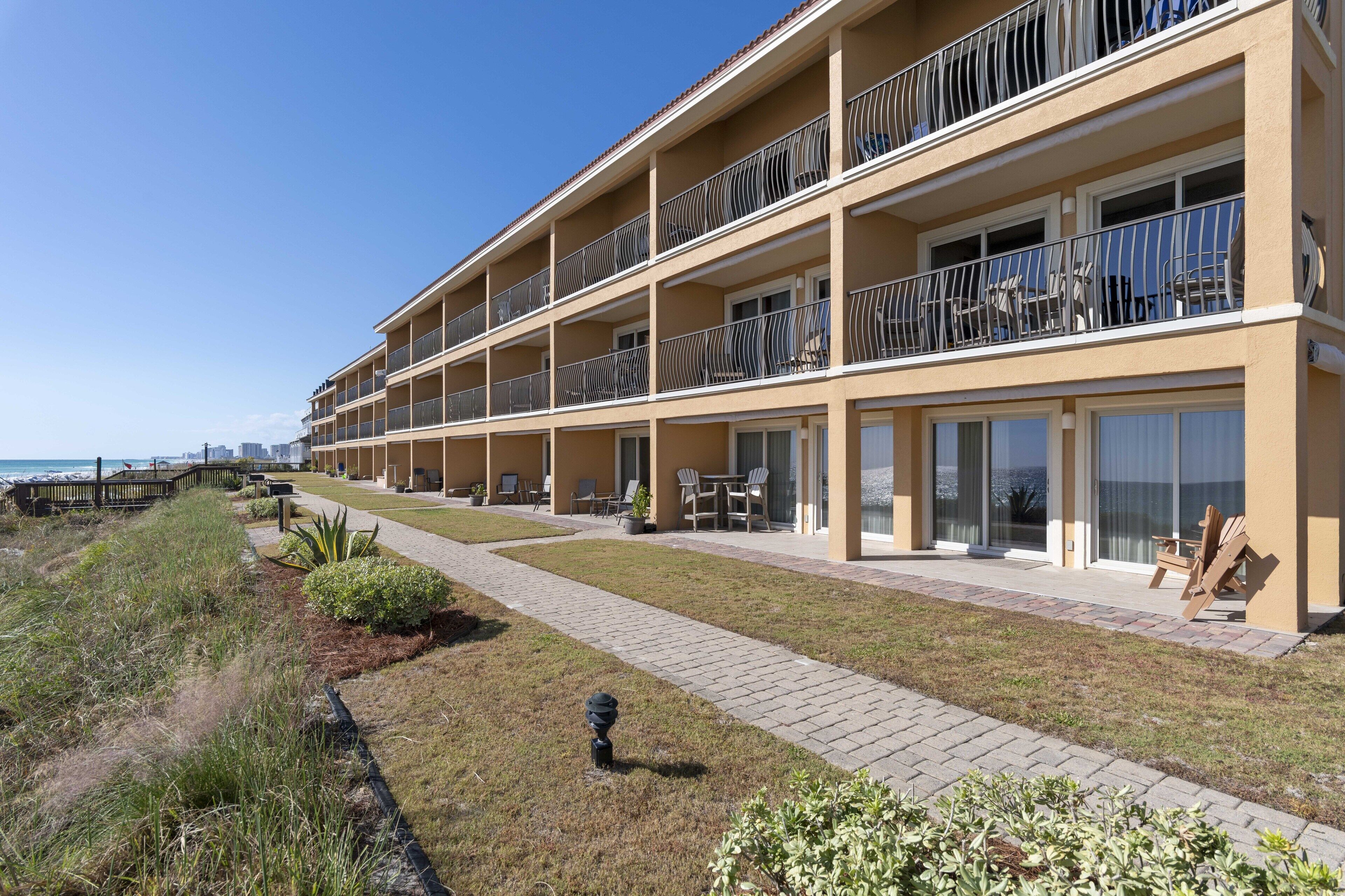 A multi-story hotel with balconies, outdoor seating, and a view of the beach.