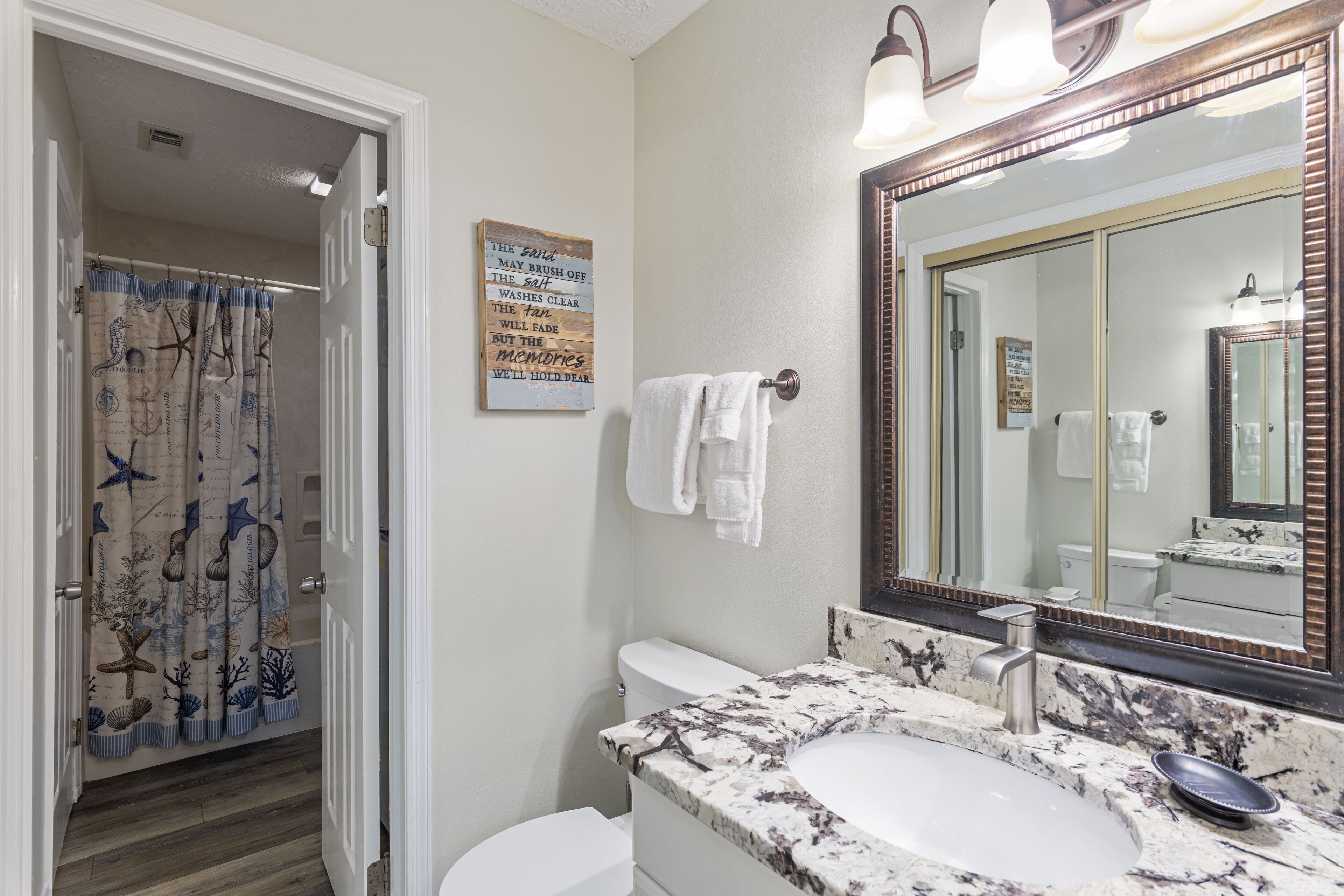 A bathroom with a shower curtain featuring a nautical theme, a white toilet, a sink with a marble countertop, and a large mirror.