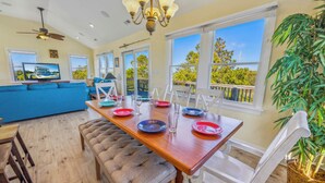 A dining area with a wooden table set for four, white chairs, and a view of the outdoors through large windows.