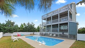 A two-story building with a pool, outdoor seating, and a white fence.