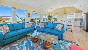 A spacious living area with two blue sofas, a glass coffee table, and a patterned rug.