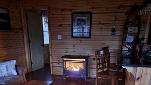 A cozy cabin interior with a wooden floor, a sofa, a dining table, and a fireplace.