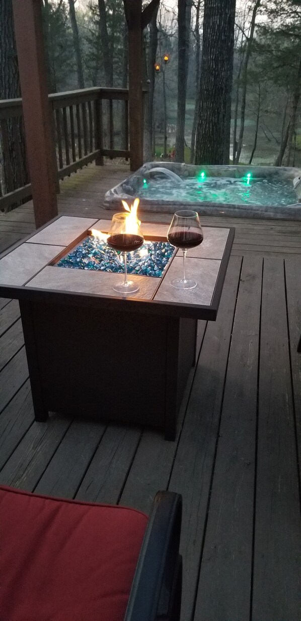 Terraza de madera con una mesa de vidrio, dos copas de vino tinto y una chimenea.