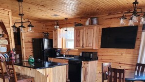 A wooden cabin interior with a kitchen, dining area, and a large TV mounted on the wall.