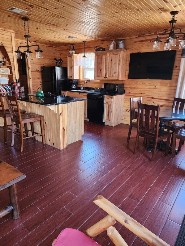 Interior de una cabaña de madera con cocina, comedor y un televisor grande montado en la pared.