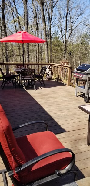 A wooden deck with outdoor furniture, including a red chair, a table, and a grill.