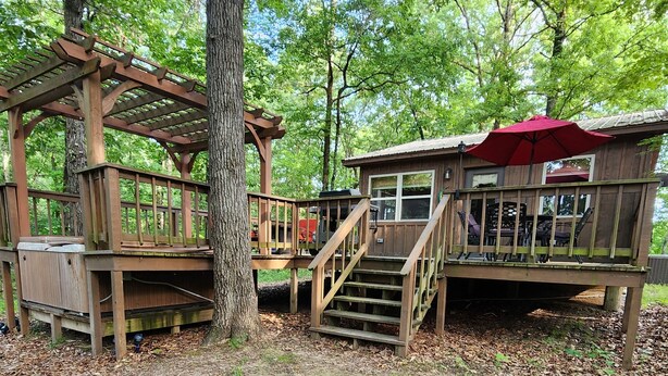 A wooden cabin with a deck, stairs, and a red umbrella.