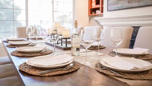 A dining table set with plates, cutlery, and wine glasses, with a bottle of wine and candles on the table.