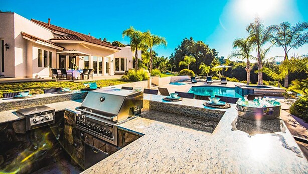 A luxurious outdoor pool area with a built-in grill and seating.