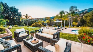 A patio area with wicker furniture, a pool, and a landscaped garden.