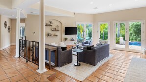 A spacious living area with a sofa set, a coffee table, and a TV mounted on the wall. There is a balcony with a pool visible through the glass doors.