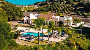 A large house with a swimming pool, surrounded by lush greenery and hills.
