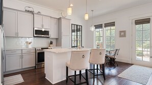 A modern kitchen with white cabinets, stainless steel appliances, and a central island with bar stools. - Spacious, golf cart included-pet friendly, short stroll to beach (Santa Rosa Beach)