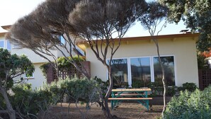 A building with a patio area featuring a wooden bench. - Birdies, Beaches and Butterflies in Pacific Grove! Pet Friendly-Premier location (Pacific Grove)