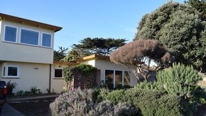 A residential property with a two-story house, a well-maintained garden with various shrubs and a large tree, and a parked car in the driveway. - Birdies, Beaches and Butterflies in Pacific Grove! Pet Friendly-Premier location (Pacific Grove)