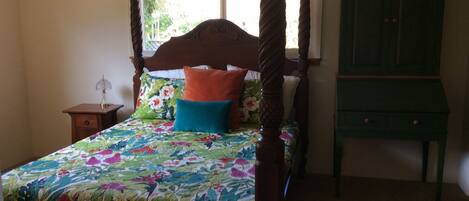 A four-poster bed with a floral bedspread, a nightstand with a lamp, and a green cabinet in a bedroom.