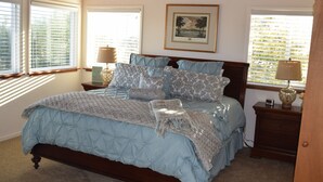 A bedroom with a large bed, two bedside tables, a framed picture on the wall, and a window with blinds. - Birdies, Beaches and Butterflies in Pacific Grove! Pet Friendly-Premier location (Pacific Grove)