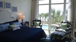 A bedroom with a large bed, two armchairs, a small table, and a view of a pool and palm trees through a large window. - 3,000 Sq. Ft 2nd Floor 4 Bed/Bath End Unit  Ocean Side (Panama City Beach)