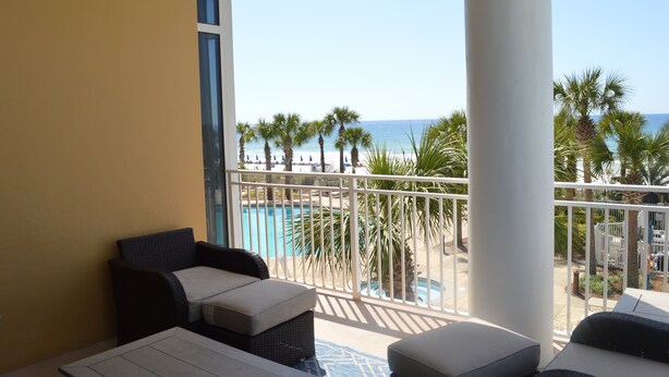 A balcony with a view of a pool and palm trees, featuring wicker furniture and a white railing. - 3,000 Sq. Ft 2nd Floor 4 Bed/Bath End Unit  Ocean Side (Panama City Beach)