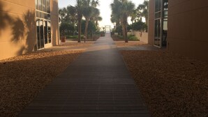 A pathway flanked by buildings with glass doors, leading to a gate. - 3,000 Sq. Ft 2nd Floor 4 Bed/Bath End Unit  Ocean Side (Panama City Beach)