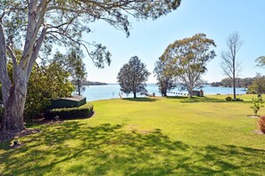 A grassy area with trees and a body of water in the background. - Edgewater Lakehouse at Morisset Memories (Morisset Park)