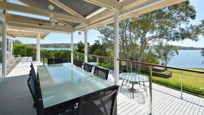 Un espace extérieur abrité, aménagé pour prendre les repas, avec une table et des chaises en verre, donnant sur un lac.