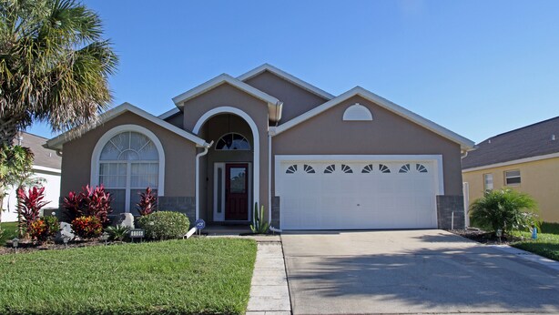 A two-story house with a garage, a front entrance with a red door, and a well-maintained lawn with various plants.
