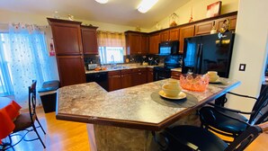 A kitchen with wooden cabinets, granite countertops, a black refrigerator, and a dining area with a chair and a table.