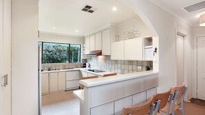 Une cuisine moderne avec des meubles blancs, un îlot central et une vue sur la verdure à l’extérieur.