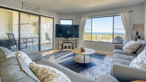 A living room with a sofa, a coffee table, a TV, and a view of the beach. - CRC 3403 - Newly Renovated Direct Ocean View (St Augustine)