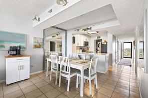 Een moderne keuken met witte kastjes, een eethoek met witte stoelen en uitzicht naar buiten.