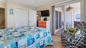 Een slaapkamer met een bed, een dressoir, een televisie en een schuifpui naar een balkon.