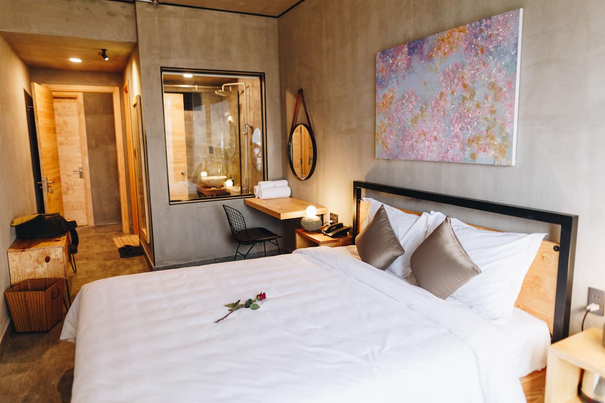 A hotel room with a large bed, a desk, a chair, a mirror, and a painting on the wall.