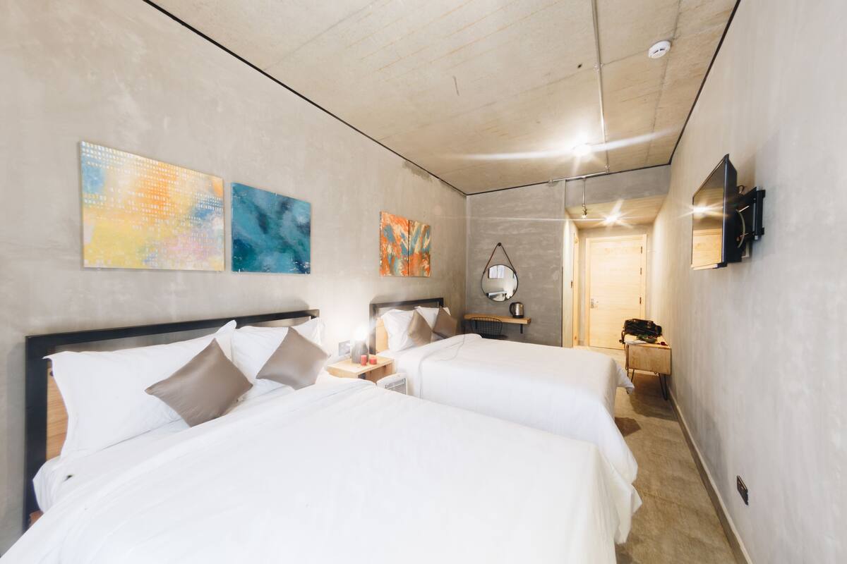 A hotel room with two beds, a TV, artwork on the walls, and a hallway leading to another room.